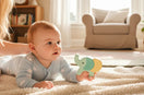 Baby liegt auf einer weichen Decke im hellen Wohnzimmer und entdeckt neugierig ein altersgerechtes Holzspielzeug