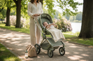 Mama spaziert mit Baby im Kinderwagen im Park – entspannter Spaziergang unterwegs mit Baby
