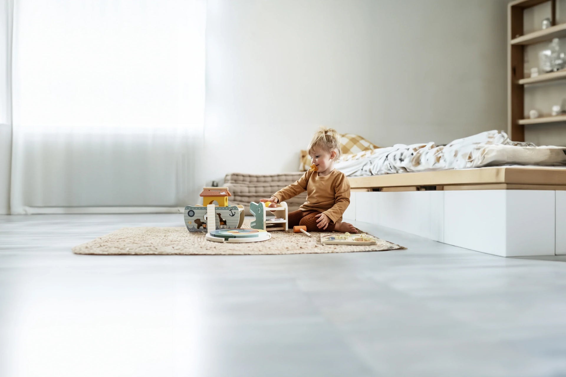 Kleinkind spielt mit Holzspielzeug im hellen Kinderzimmer auf einem Teppich, geeignet für Babys und Kleinkinder