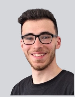 Porträtfoto des IT- und Technikverantwortlichen von BabyLions mit schwarzer Brille, kurzem dunklem Haar und schwarzem T-Shirt vor einfarbig grauem Hintergrund – professionelle Vorstellung im Teamprofil.