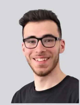 Porträtfoto des IT- und Technikverantwortlichen von BabyLions mit schwarzer Brille, kurzem dunklem Haar und schwarzem T-Shirt vor einfarbig grauem Hintergrund – professionelle Vorstellung im Teamprofil.