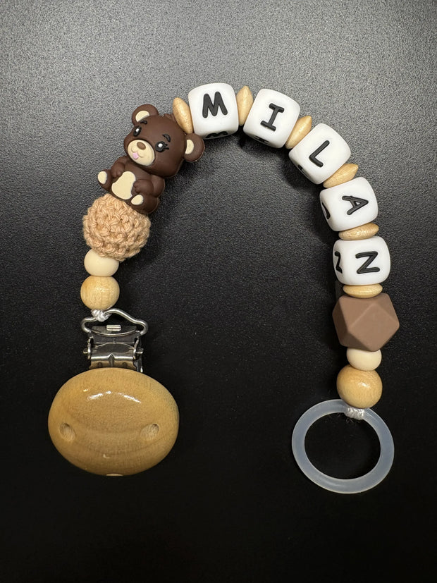 Detailansicht der personalisierten Schnullerkette Bär mit Namen von BabyLions® mit Teddy-Motiv, Holzclip, Silikonring sowie Silikon- und Holzperlen in Natur- und Brauntönen