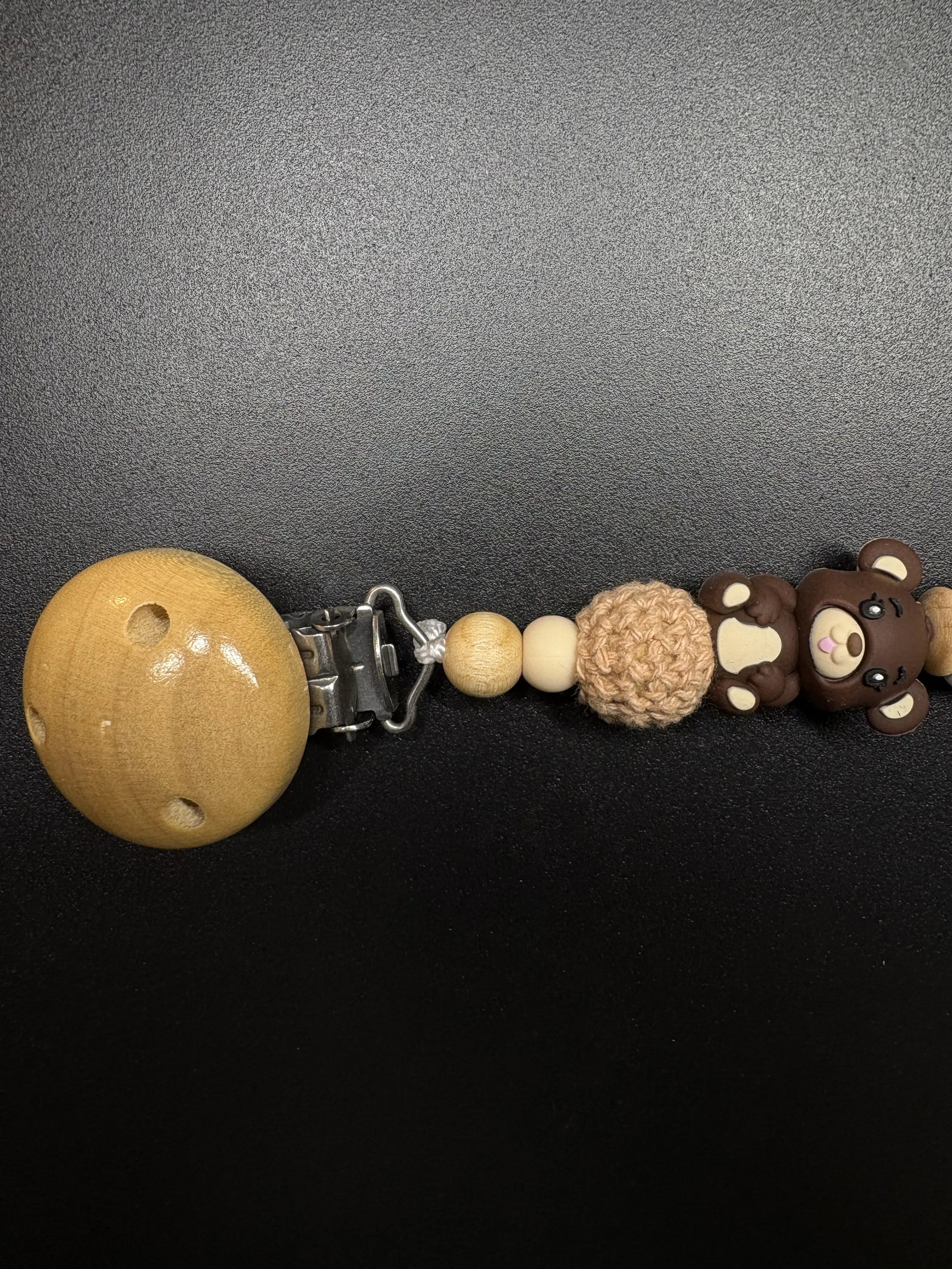 Seitenansicht der personalisierten Schnullerkette Bär mit Namen von BabyLions® mit Teddy-Motiv, gehäkelter Perle, Holzclip sowie hochwertigen Silikon- und Holzperlen in Natur- und Brauntönen