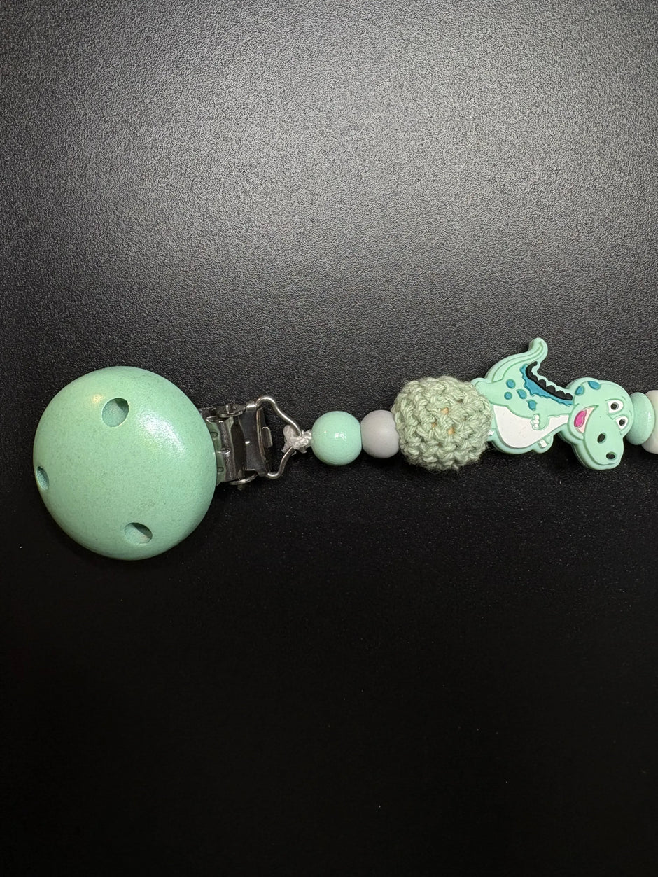 Seitenansicht der personalisierten Schnullerkette Dino mit Namen von BabyLions® mit Dino-Motiv, gehäkelter Perle, Holzclip und hochwertigen Silikon- sowie Holzperlen in Mint
