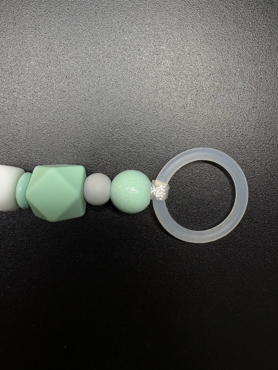 Nahaufnahme des Silikonrings der personalisierten Schnullerkette Dino mit Namen von BabyLions® mit mintfarbener Silikonperle, Holzperle und hochwertigem Schnulleradapter