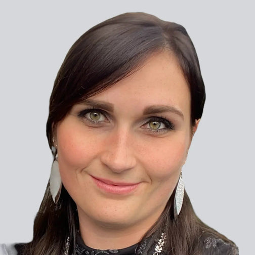 Porträtfoto der Assistentin der Geschäftsführung von BabyLions mit dunklem Haar, silbernen Ohrringen und schwarzer Bluse vor einfarbig grauem Hintergrund – professionelle Vorstellung im Teamprofil.