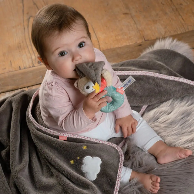 Baby Kuscheldecke Bär grau mit Spielzeug – Baby sitzt eingekuschelt und spielt mit Greifring