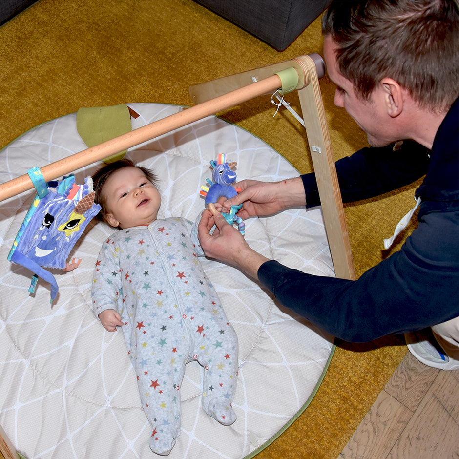 Baby liegt unter Spielbogen mit Zebra Activity Spielzeug – Motorikspielzeug und Beißring für Babys
