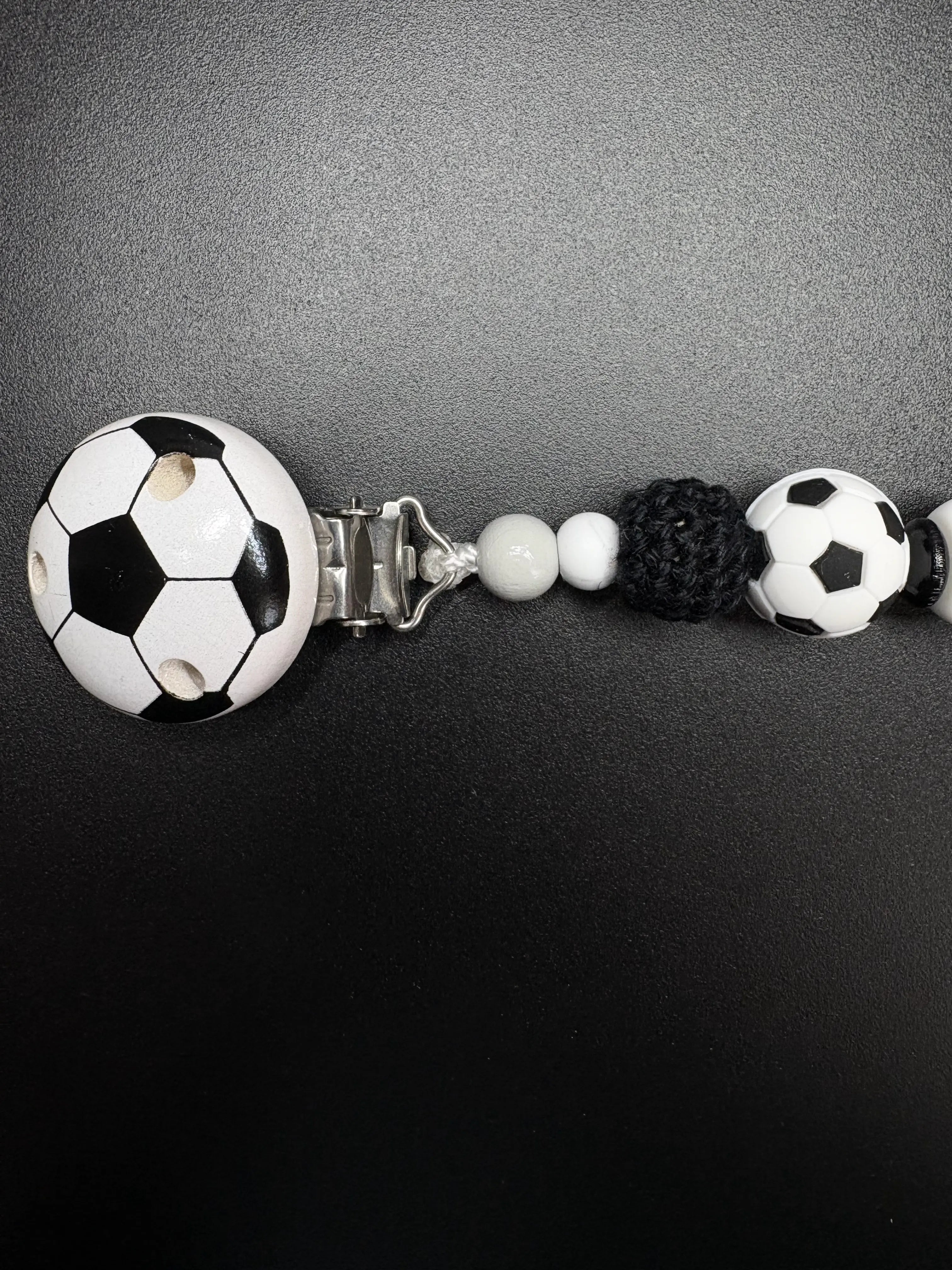Detailaufnahme des Fußballclips und der Häkelperle der personalisierten Schnullerkette Kilian in Schwarz Weiß