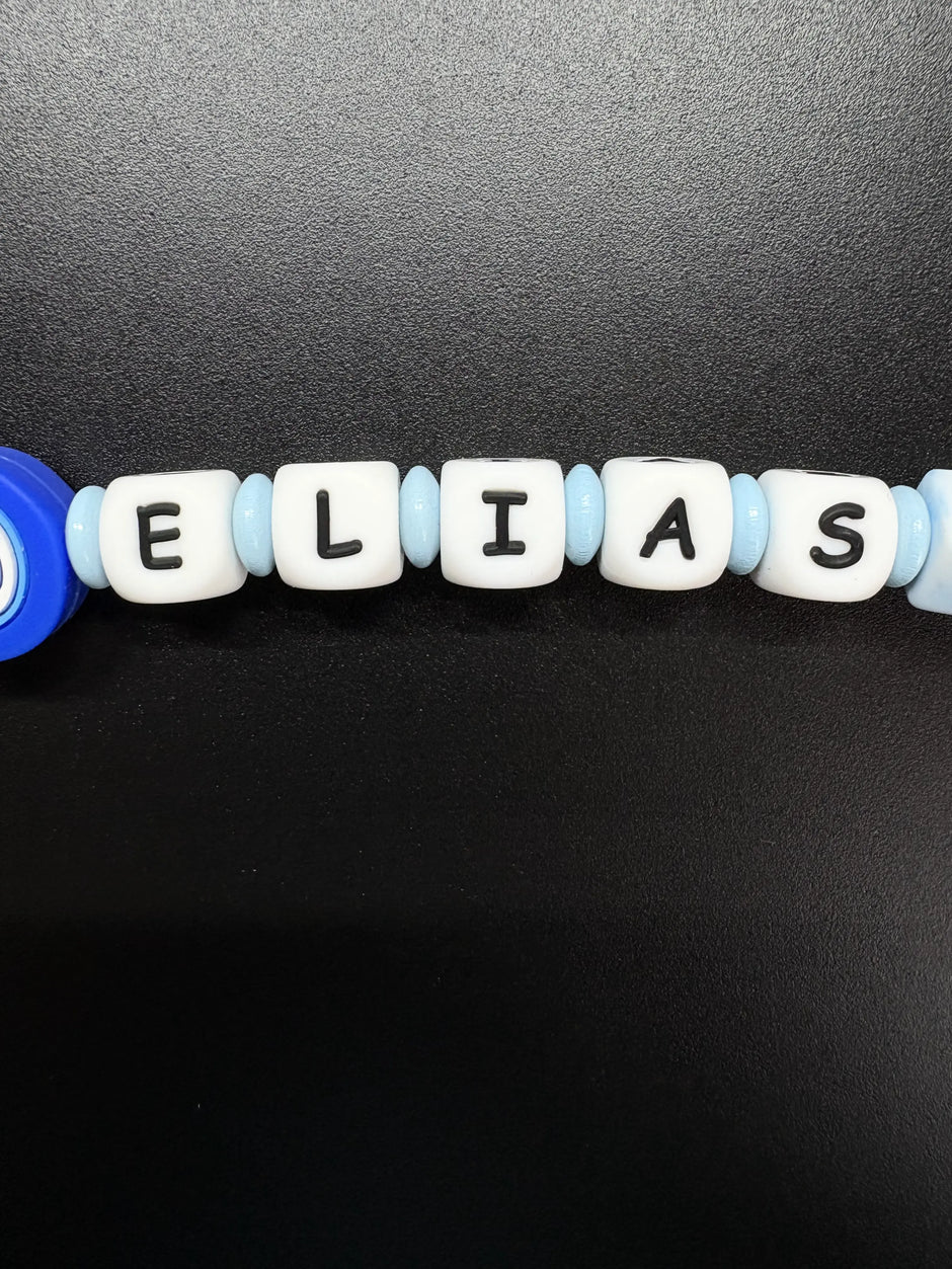 Detailaufnahme des Namens Elias auf einer personalisierten Schnullerkette in Hellblau und Weiß