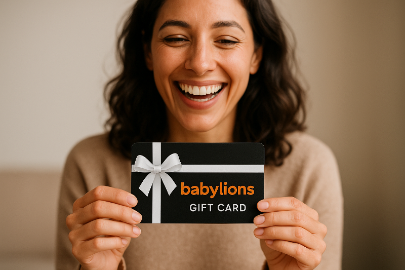 Eine glückliche Frau mit einem warmen Lächeln hält eine Gutscheinkarte von BabyLions in der Hand. Sie wirkt begeistert und voller Vorfreude. Die Gutscheinkarte ist modern gestaltet – mit schwarzem Hintergrund, weißer Schleife und dem orangefarbenen Schriftzug „babylions“.