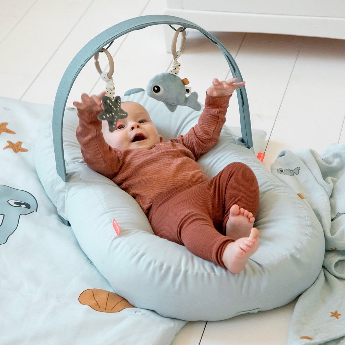 Baby spielt mit Hängespielzeug Wally und Seestern am Aktivitätsbogen auf weicher Spielunterlage