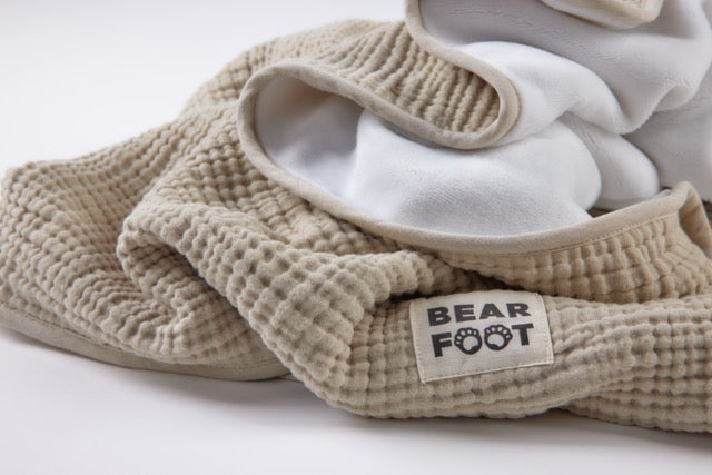 Gefaltete sandfarbene Musselin-Babydecke mit weicher Fleece-Innenseite und BEARFOOT-Label – kuschelig, atmungsaktiv und ideal für Neugeborene