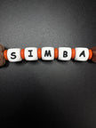 Detailaufnahme der personalisierten Schnullerkette Simba mit weißen Namensperlen und orangefarbenen Silikonringen