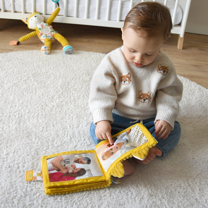 Kleinkind sitzt auf Teppich und blättert in gelbem Stoff-Fotoalbum von Les Déglingos
