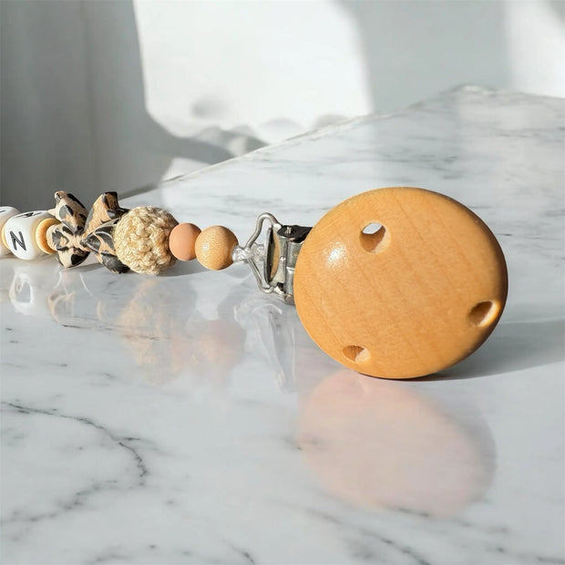Nahaufnahme einer personalisierten Schnullerkette im Leopard-Design mit Holzclip und Perlen von BabyLions